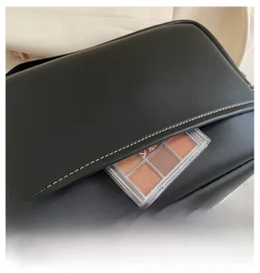 Detail of black leather crossbody bag front pocket holding an eyeshadow palette