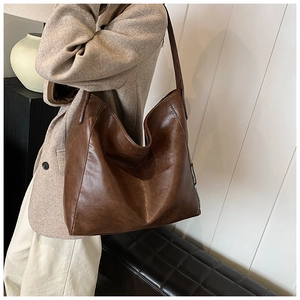 Close-up of deep brown leather tote bag worn with a beige coat in a street style setting
