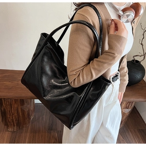Sac cabas en similicuir noir brillant porté par un mannequin dans un intérieur chic