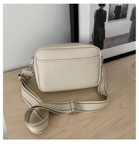 Detail of a minimalist cream crossbody bag with wide striped canvas strap on wooden surface