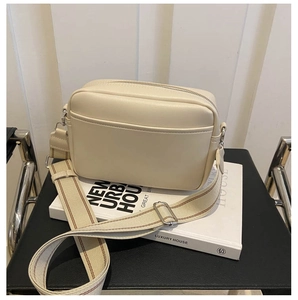 Detailed close-up of cream white camera bag with striped canvas strap on a white book