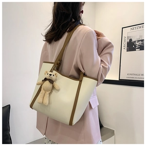 Contrast tote bag in cream and brown with bear charm worn by a model in a suit
