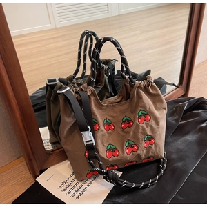 Detailaufnahme von Pixel-Kirschstickerei auf brauner Canvas-Tasche mit gewebten Griffen
