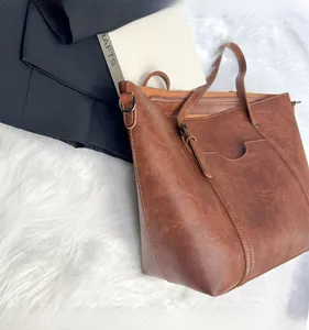 Detail of vintage brown leather tote bag showing high-quality stitching and front pocket