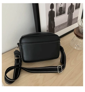 Detail view of black crossbody camera bag with white contrast stitching and wide strap