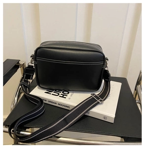Detail of black crossbody camera bag with contrast white stitching and wide woven strap