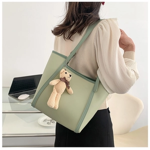Green contrast tote bag with plush bear charm shown on model in modern office setting