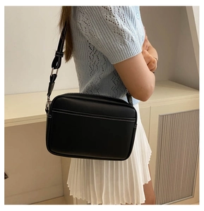 Detail of black crossbody bag with white contrast stitching on a model in a minimal setting