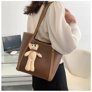 Detail view of large dark brown tote bag with contrast piping and cute plush bear charm