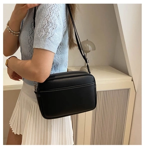 Close-up of black crossbody camera bag with contrasting white stitching and silver hardware