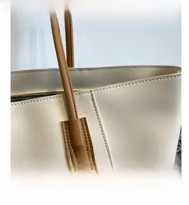 Close-up of fine stitching detail on cream tote bag with brown leather handles