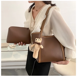Detailed view of brown leather tote bag with small bear charm and matching inner pouch