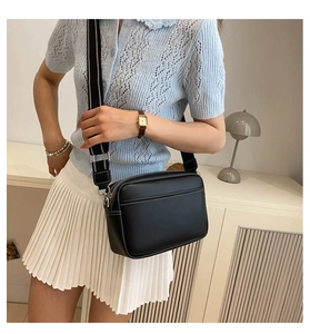 Detail of black crossbody bag featuring white contrast stitching and a striped strap