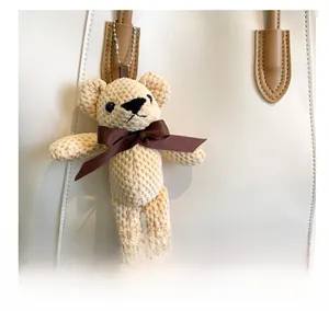 Close-up of cream knit bear charm with brown bow on a white leather tote bag