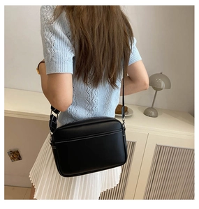 Detail of black crossbody bag with white contrast stitching and adjustable wide strap