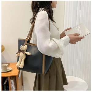 Detail of color-block tote bag with bear charm on a female model in cozy library setting