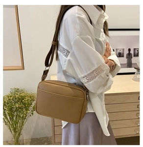 Detail of khaki PU camera bag showing white contrast stitching and wide fabric strap