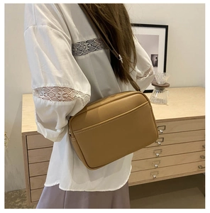Detail of khaki crossbody bag with white stitching shown on a model in a home setting