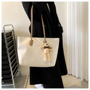Detail of cream tote bag with brown straps and cute knitted bear charm for daily commute