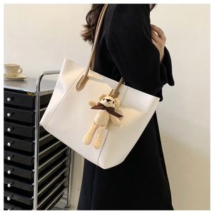 Detail of white leather tote bag with brown straps and cute beige bear pendant charm