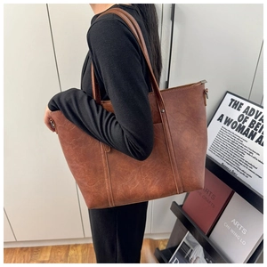 Brown vintage tote bag shown on model's shoulder with smooth leather texture detail