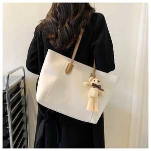 Detailed view of beige tote bag with brown leather straps and cute teddy bear charm