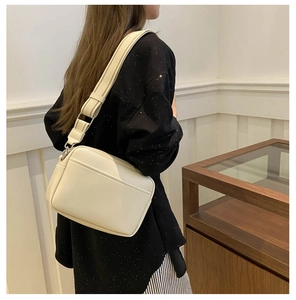 Side view of cream crossbody camera bag with striped wide textile shoulder strap on model