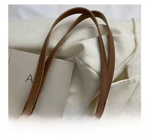 Detail view of the beige tote bag with premium brown leather handles and textured fabric