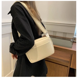 Side view of beige leather crossbody bag with wide textile strap and silver buckle