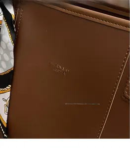 Close-up of brown leather tote bag with gold logo embossing and printed silk scarf