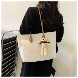 Close-up of cream large tote bag with brown leather straps and a plush bear pendant