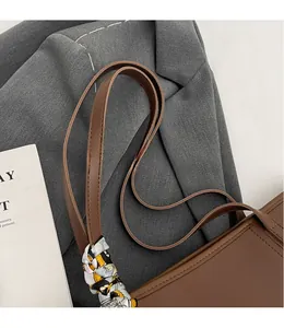 Detail of a brown leather tote shoulder strap with a decorative floral silk scarf wrap