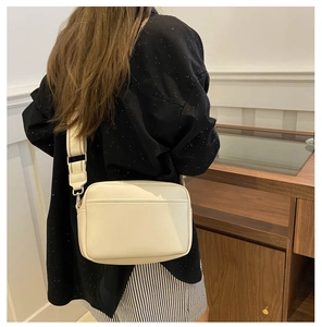 Detail of cream rectangular crossbody bag with wide strap and front pocket on striped dress