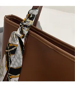 Detail view of brown leather tote bag with silk scarf accessory and fashion engraving