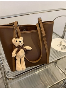 Modern two-tone brown tote bag with cute knit bear charm on a stylish display shelf