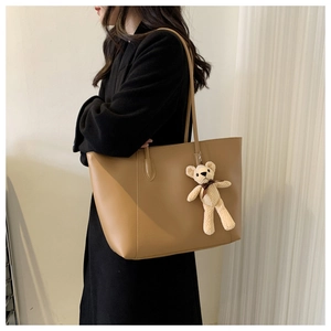 Large khaki tote bag with plush bear charm worn on shoulder over black wool coat