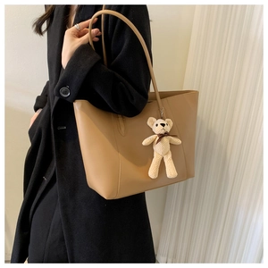 Side view of large khaki tote bag with plush bear charm on black coat model