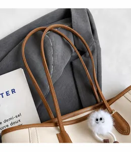 Detail view of cream tote bag handle with brown straps and cute furry charm accessory