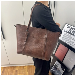 Close-up of vintage brown leather tote bag with curved pocket and metallic hardware detail