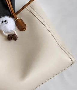 Detail of beige faux leather tote with brown handles and a cute plush monster charm