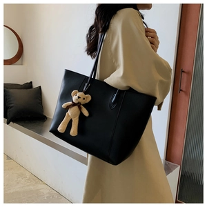 Detail of black leather tote bag with a cute brown bear pendant on a shoulder strap