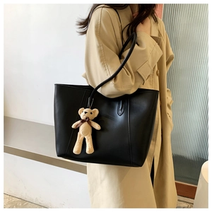 Close-up of black PU leather tote bag with a beige knit bear charm on shoulder