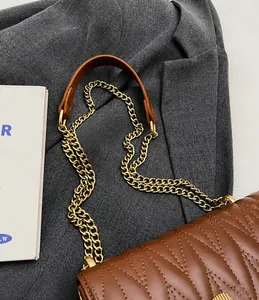 Detailed close-up of brown leather strap with golden metal chain and V-shaped quilting