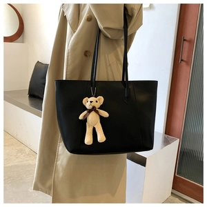 Detail of a black matte leather tote bag featuring a cute beige knit bear charm