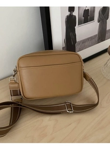 Minimalist tan leather crossbody bag with wide strap and white stitching on wood surface