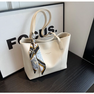 Close-up of cream leather tote bag with printed letters and elegant silk scarf on handle