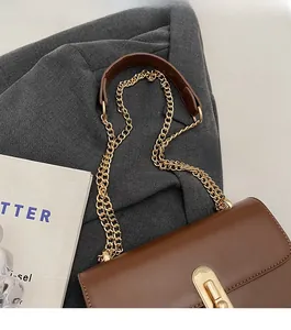 Detail of brown leather flap bag with gold chain strap on a grey suit fabric