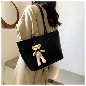 Close-up of black leather tote bag with a cute knit bear charm in a minimalist interior
