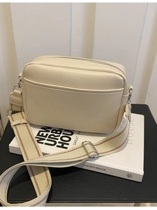 Minimalist cream leather crossbody bag with striped canvas strap on a white stand
