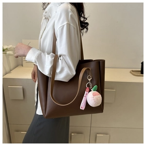 Detail of dark brown faux leather tote bag with a pink peach plush charm and sweet strap